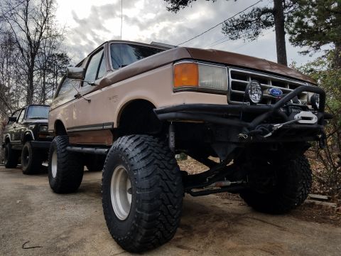 1988 Ford Bronco - This heavily modified SUV features a prominent aftermarket bumper and large off-road tires, suggesting it is from the late 1980s.