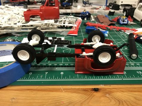 1989 Ford Bronco - A model truck chassis and red cab are assembled on a cutting mat, with tape and other model parts visible in the background.