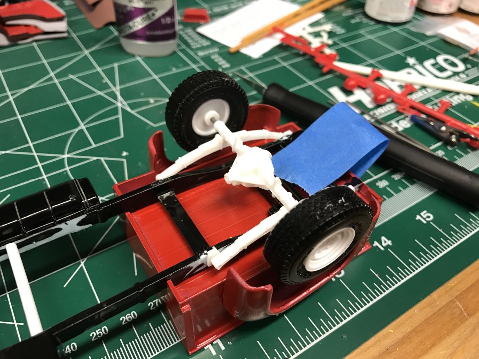 Model truck chassis with red bed, black frame, and white suspension parts on a green cutting mat