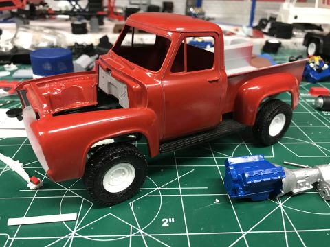 1989 Ford Bronco - A partially assembled red model truck sits on a cutting mat, with its hood open and a separate engine model nearby.