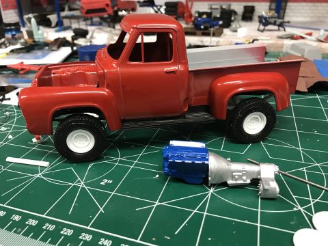 1989 Ford Bronco - A red 1953 Ford F-100 model truck is shown on a green cutting mat, with its engine and transmission components laid out separately.