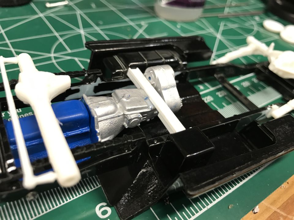 Model car chassis with blue engine and silver transmission assembly on a cutting mat