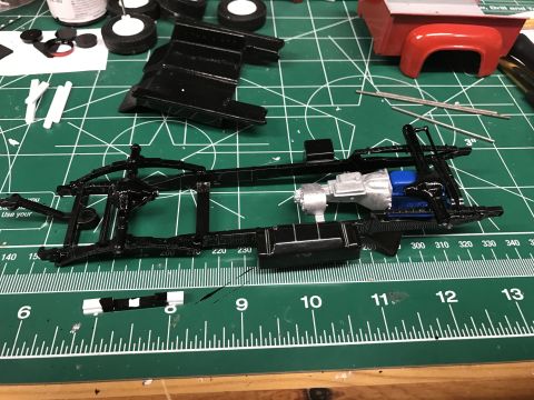 1989 Ford Bronco - A model truck's chassis, engine, and transmission are assembled on a green cutting mat with rulers.