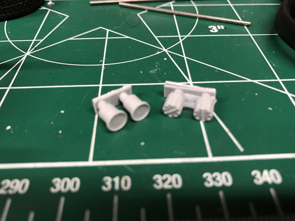 Two model exhaust pipes on a green cutting mat with ruler markings