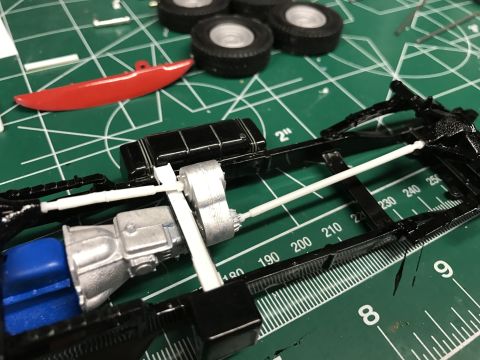 1989 Ford Bronco - A model car chassis with engine components and drive shafts is assembled on a cutting mat with loose parts.