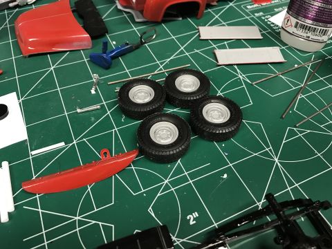 1989 Ford Bronco - Model car parts, including tires and red body pieces, are laid out on a green cutting mat, suggesting assembly in progress.