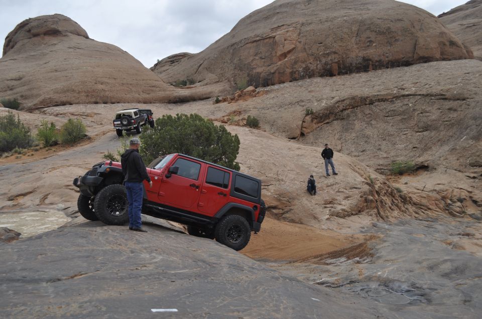 Red Jeep Wrangler on rocky terrain with a white Jeep Cherokee in the background