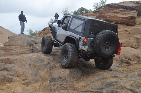 1991 Ford Bronco - A silver Jeep Wrangler tackles a challenging rocky trail with two people observing.