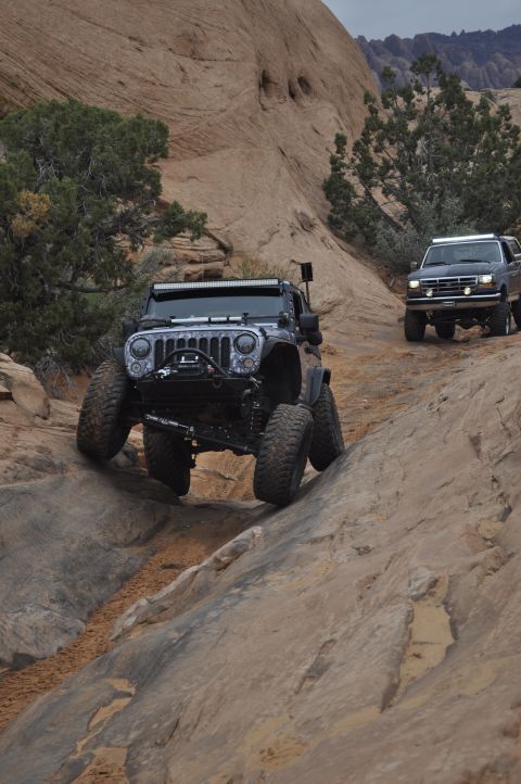 1991 Ford Bronco - Two modified off-road vehicles navigate a challenging rocky terrain in a desert landscape.