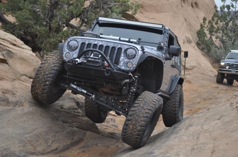 1991 Ford Bronco - A heavily modified Jeep Wrangler navigates a rocky trail, with another vehicle following behind.
