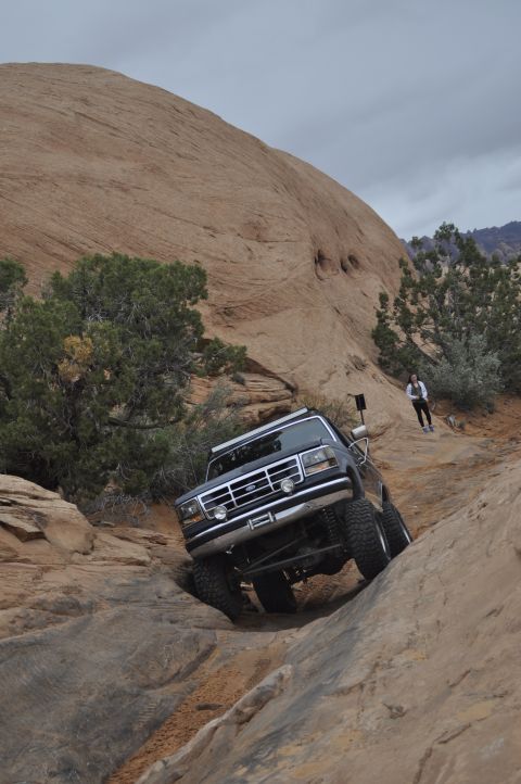 1991 Ford Bronco - A lifted Ford truck navigates a steep, rocky off-road trail under a cloudy sky.