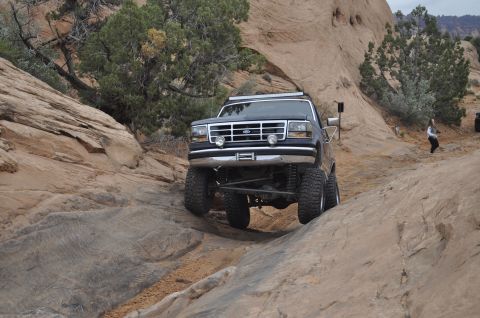 1991 Ford Bronco - A black Ford Bronco navigates a challenging rocky trail with its front end angled towards the camera.
