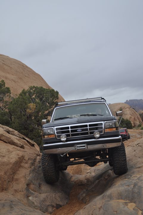 1991 Ford Bronco - A dark blue Ford Bronco navigates a rocky off-road trail under an overcast sky.