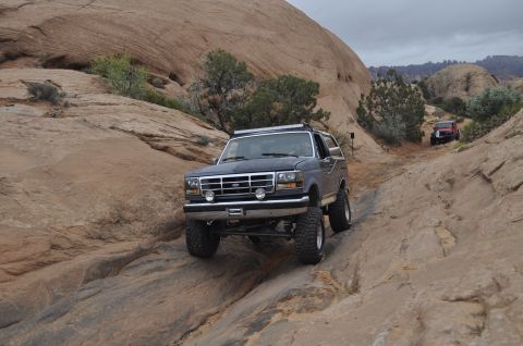 1991 Ford Bronco - A lifted Ford Bronco navigates a challenging rocky terrain, with another vehicle following in the distance.
