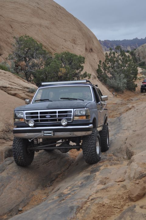 1991 Ford Bronco - A dark blue Ford Bronco navigates a challenging rocky terrain with a winch and light bar.