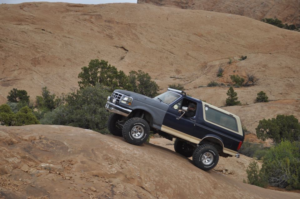 1991 Ford Bronco climbing a steep, rocky hill with sparse vegetation and a sandstone landscape