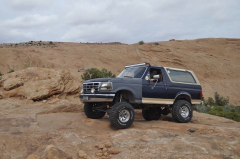 1991 Ford Bronco - This lifted Ford Bronco navigates a rocky, desert landscape under a cloudy sky.