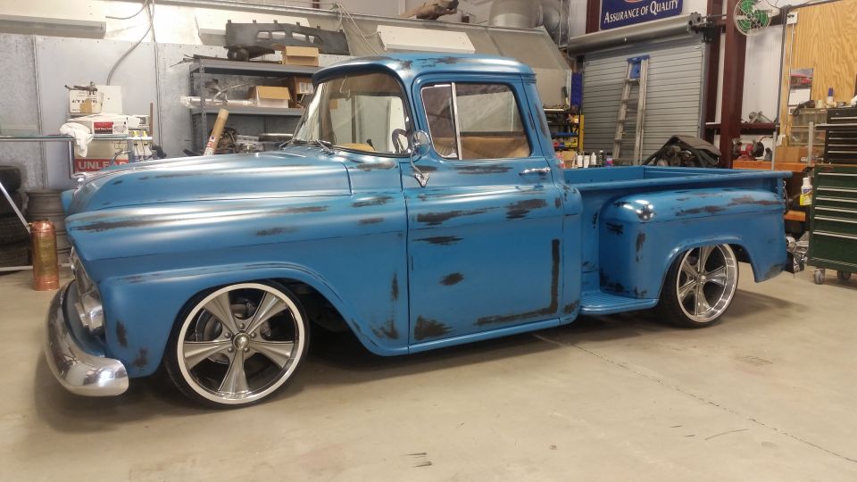 Blue pickup truck with custom wheels and a distressed paint job, parked in a garage