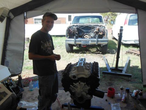 1984 Ford Bronco - A man stands next to a newly rebuilt engine, with a truck in the background missing its engine.