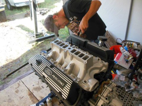 1984 Ford Bronco - A man works on a Ford Racing engine part, likely a V8, on an engine stand.