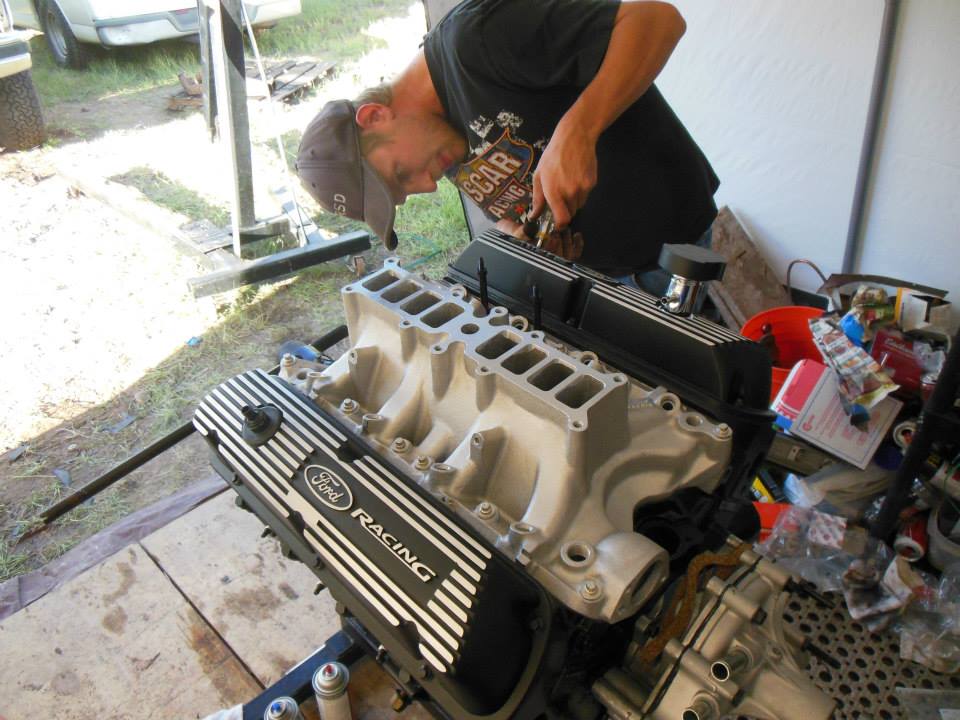Ford Racing valve cover and intake manifold on engine stand, man working on it