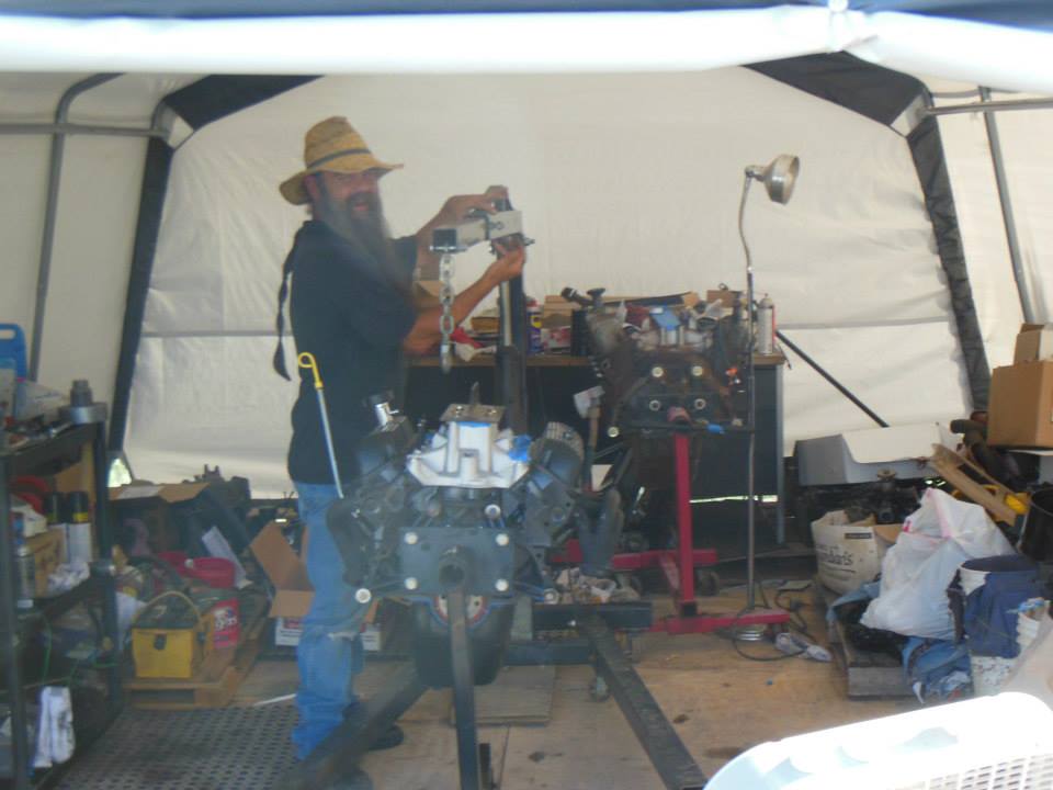 Man in straw hat works on engine in garage. Another engine is on a stand nearby