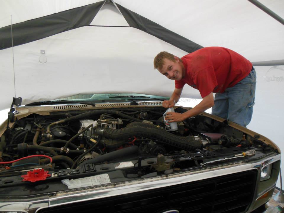 Man in red shirt pouring fluid into engine bay of a truck