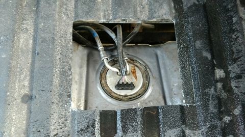 1992 Ford Bronco - Fuel pump assembly accessed through a cut-out in a textured metal surface, with visible hoses and wiring.