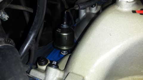 1976 Ford Ranchero - Close-up view of an engine intake manifold with a small, cylindrical part attached. Text is visible on the component.