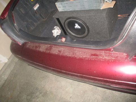 2004 Ford Crown Victoria - The trunk of a car shows a subwoofer installation and some clutter, with a dusty rear bumper.