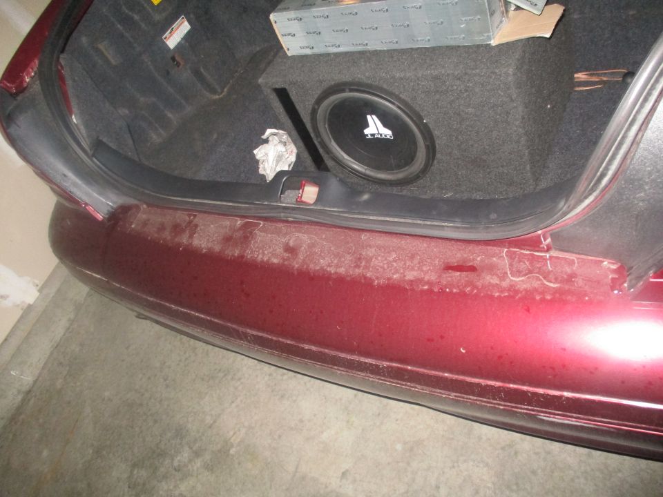 Car trunk with a JL Audio subwoofer box and some boxes stacked on top. The bumper is dirty