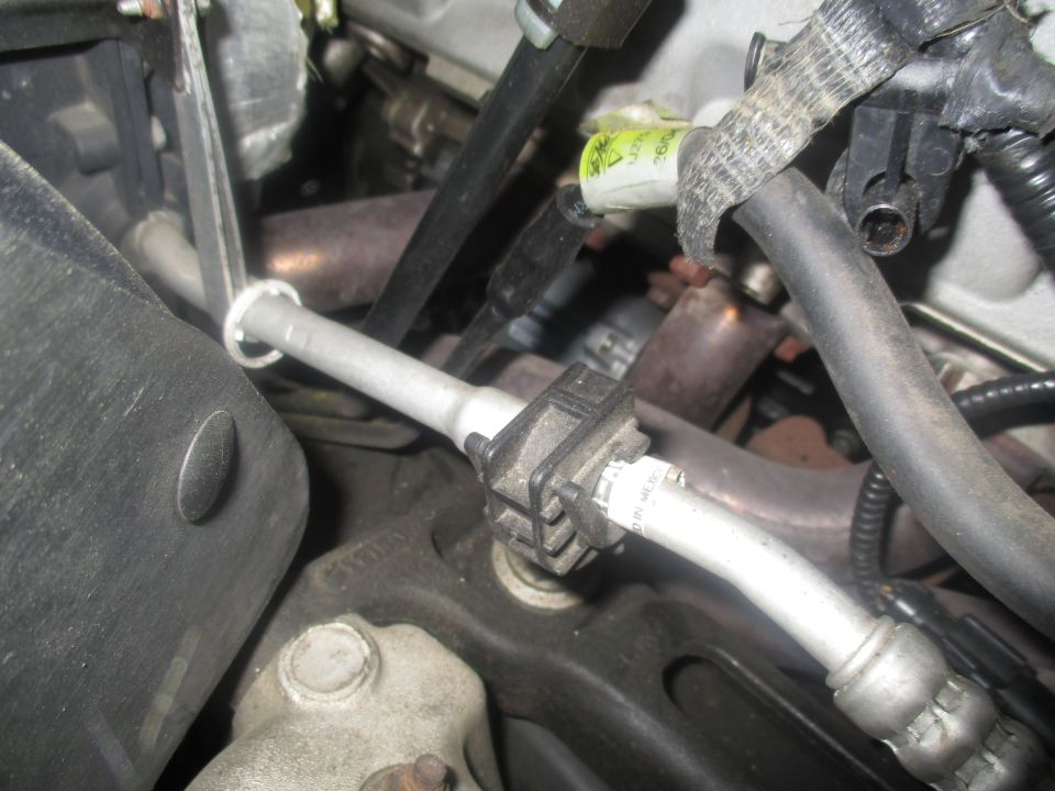 Engine bay with metal pipes and hoses, some with fabric wrap. A black sensor is attached to a pipe
