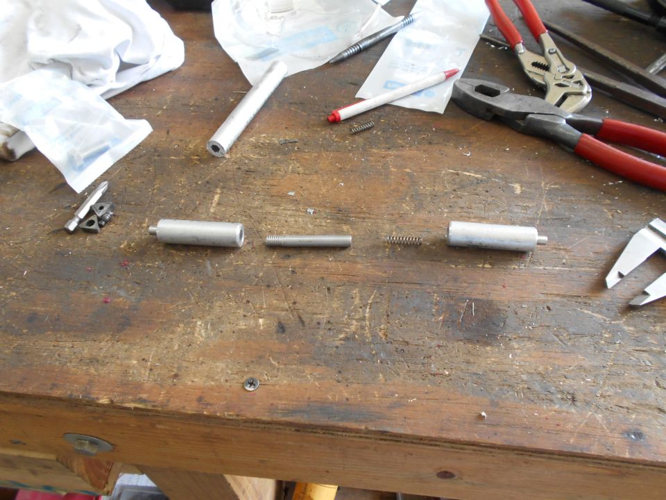 Disassembled metal cylinder parts and springs laid out on a wooden workbench with tools nearby
