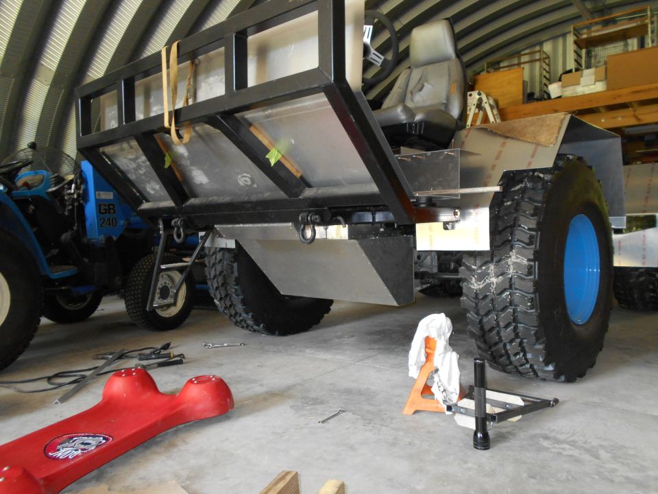 Custom vehicle with large tires and cargo bed, blue tractor in background