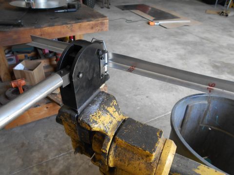 1992 Ford Bronco - A metal stock is being bent using a specialized tool attached to a yellow vise in a workshop setting.