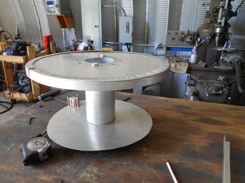 1992 Ford Bronco - A large metal spool sits on a workbench, accompanied by a tape measure and a pencil, in what appears to be a workshop setting.