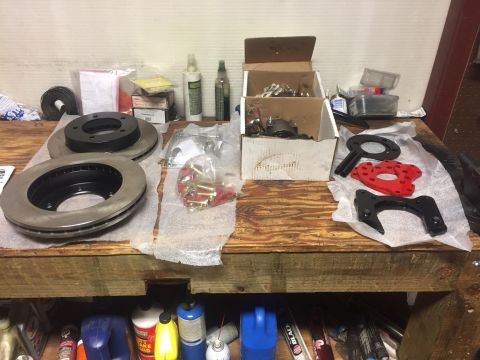 1982 Ford Bronco - Two brake rotors with black hubs are laid out on a wooden workbench, along with various brake components and hardware in boxes and bags. Be…