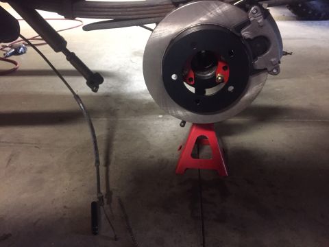 1982 Ford Bronco - A close-up view of a vehicle's rear brake assembly, including the rotor, caliper, and brake line, supported by a red jack stand.
