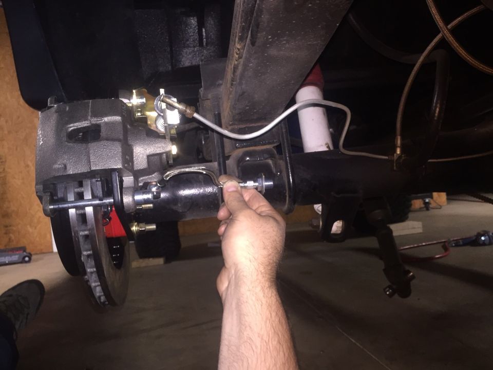 Close-up of a hand adjusting a brake caliper on a vehicle's rear axle.