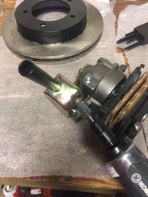 1982 Ford Bronco - A close-up view of brake components, including a brake rotor, caliper, and brake pads, being worked on with a rotary tool.