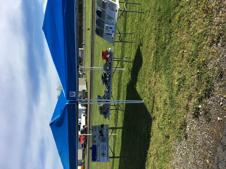 Engine parts displayed under a blue canopy tent at an outdoor event.