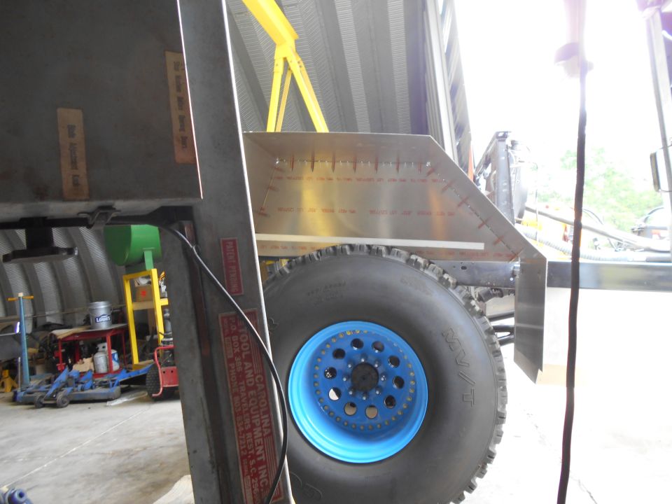 Close-up of a large off-road tire with a blue rim and a metal measurement plate on a vehicle frame.