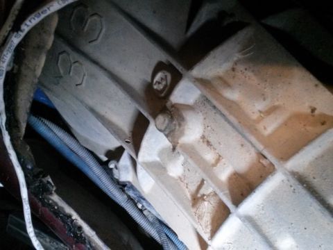 1996 Ford Bronco - Close-up view of the underside of a vehicle, showing a cast metal component with hexagonal markings and a bolt. Electrical wiring and a blu…