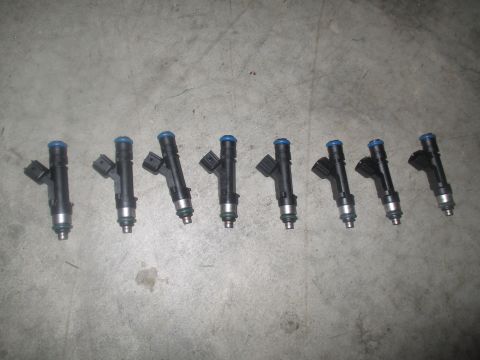 2004 Ford Crown Victoria - Eight fuel injectors with blue tops are laid out in a line on a concrete surface. The injectors are black with silver accents near the bott…