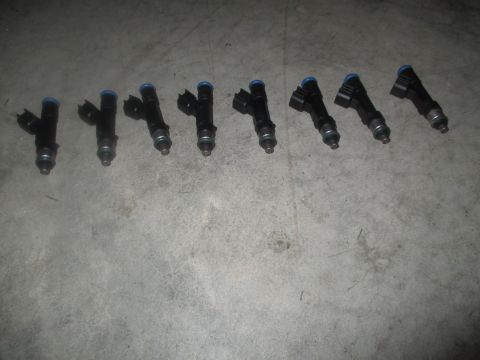 2004 Ford Crown Victoria - Eight black fuel injectors with blue tops are laid out diagonally on a concrete surface. The injectors are arranged in a line from the bott…