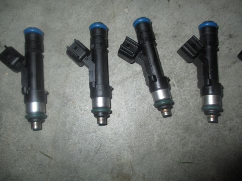 2004 Ford Crown Victoria - Four black fuel injectors with blue caps and silver tips are laid out on a gray concrete surface. Each injector has a black electrical conn…