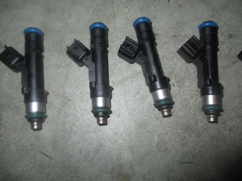Four black fuel injectors with blue caps and silver tips on a gray concrete surface.