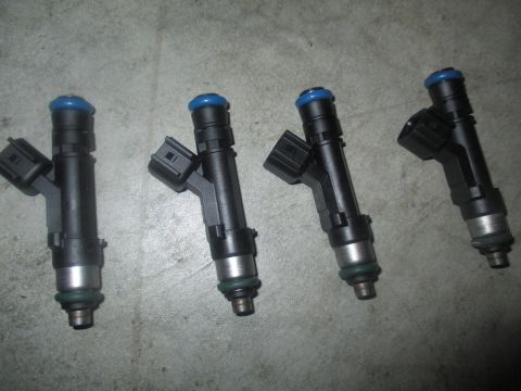 2004 Ford Crown Victoria - Four black fuel injectors with blue tops are laid out on a gray concrete surface. The injectors are oriented vertically with their tops fac…