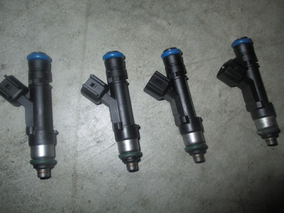 Four black fuel injectors with blue tops on a gray concrete surface.
