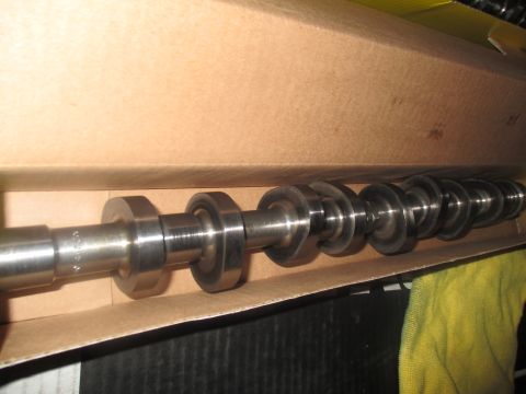 2004 Ford Crown Victoria - A camshaft is shown lying horizontally inside a cardboard box. The camshaft has multiple lobes and appears to be made of metal.